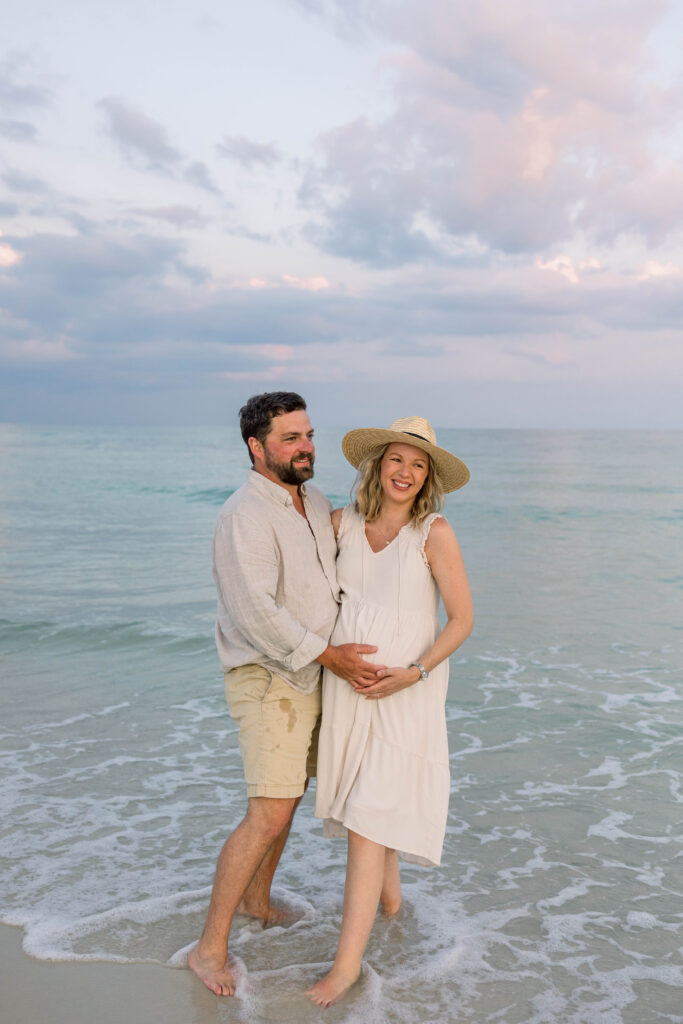 Pregnant Mom with husband in sundress and sun hat standing on Pensacola Beach