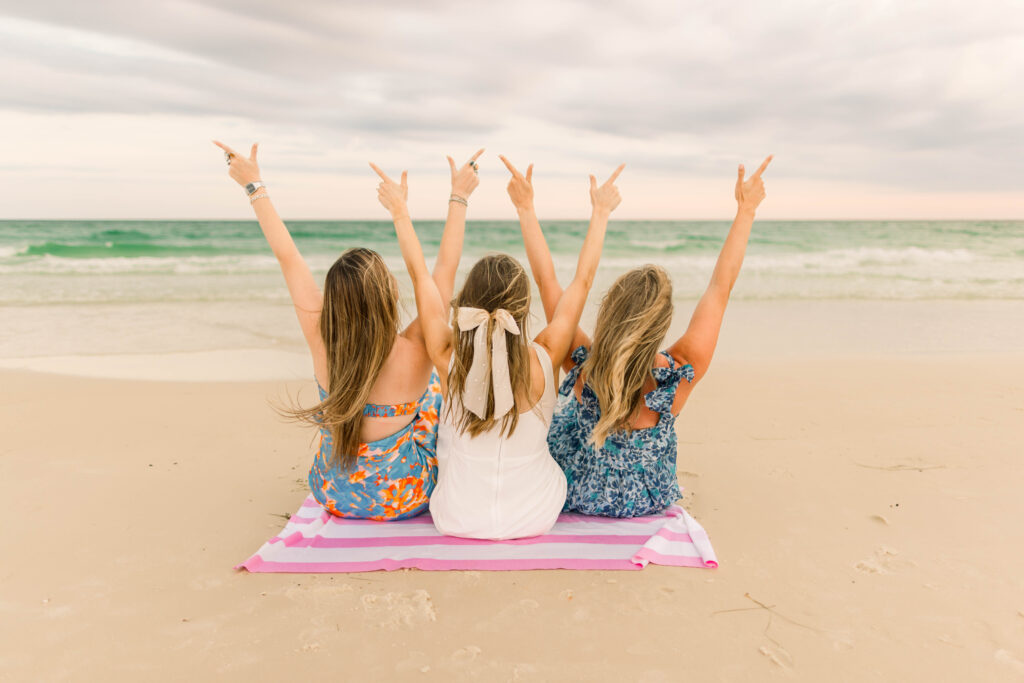 Three girls on the beach making the Texas hook em horns sign in colorful outfits.