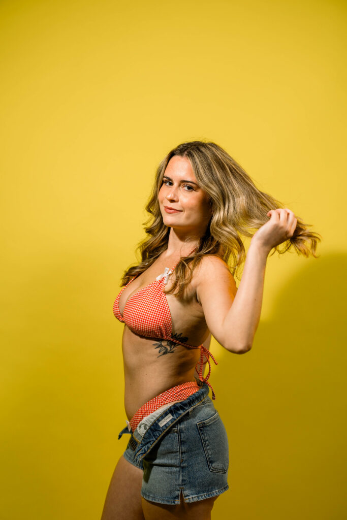 A girl in a photo studio doing a summer photoshoot in a red bikini with a bright yellow backdrop